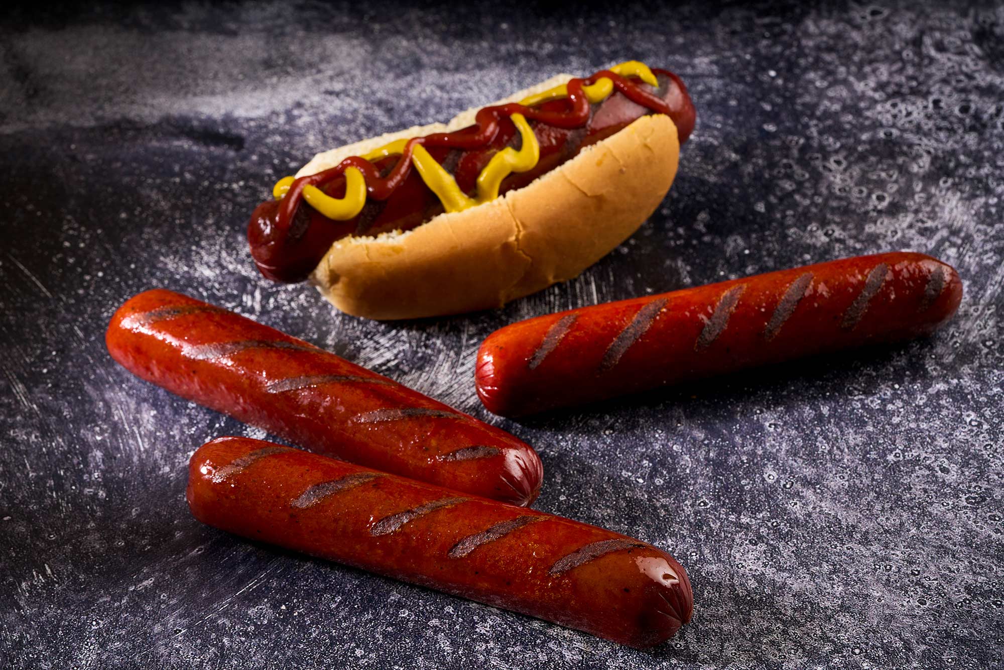 Wagyu franks with a charred finish, served alongside a hot dog topped with ketchup and mustard, showcasing premium Rosewood Beef products.