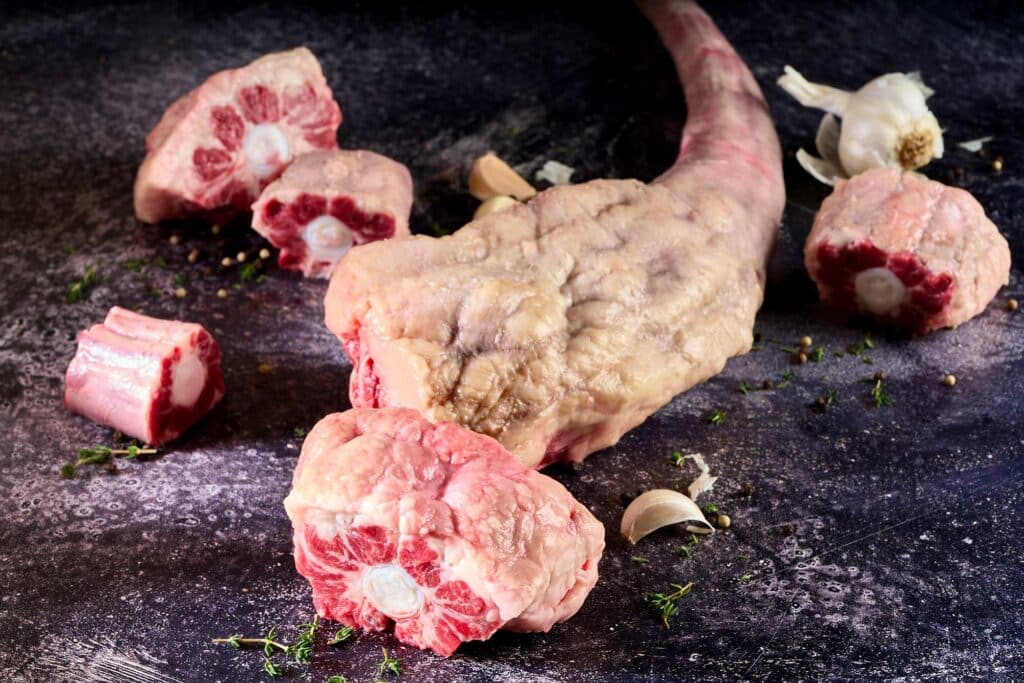 Bone-In Wagyu oxtail with rich marbling, segmented joints, surrounded by garlic and herbs, showcasing premium offal for slow-cooking and braising.