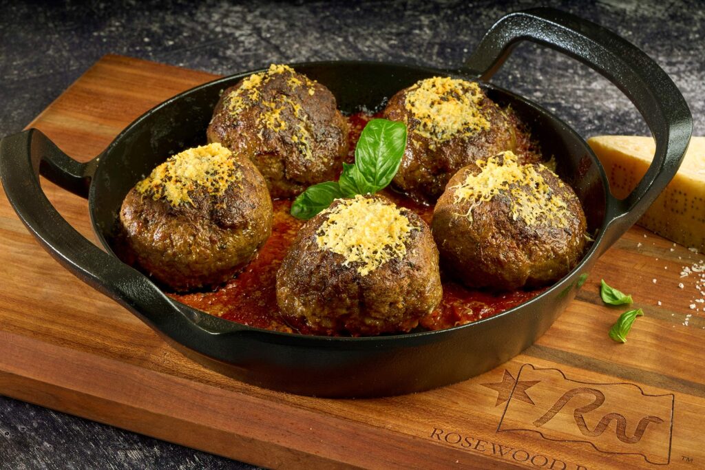 Wagyu beef meatballs topped with cheese and basil, served in a cast iron skillet with marinara sauce, highlighting premium beef offerings from Rosewood Beef.