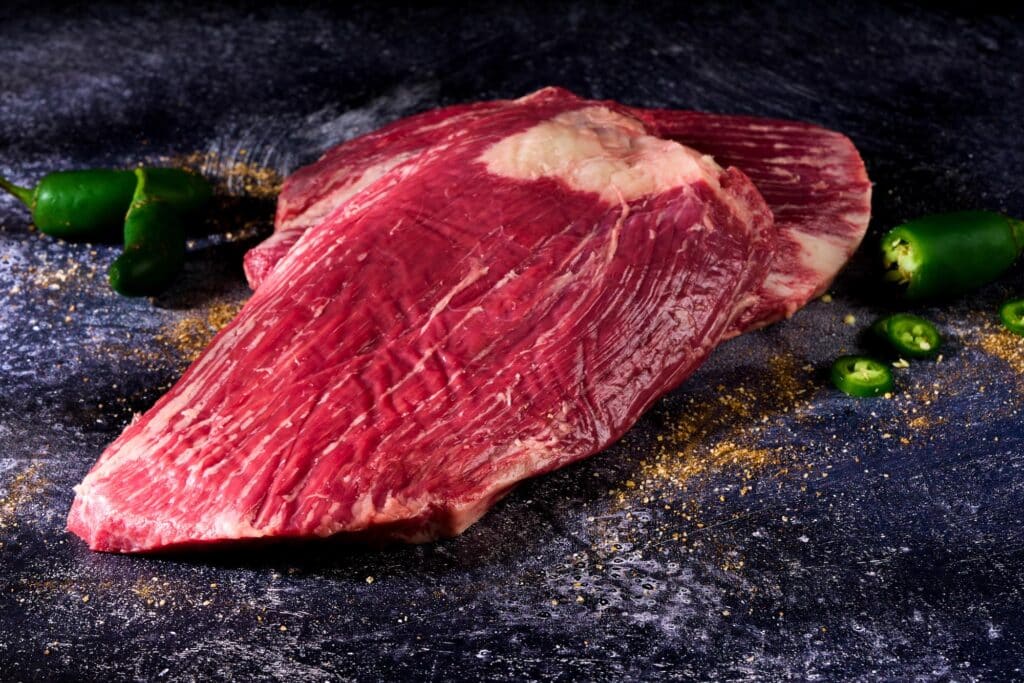 Wagyu flank steak showcasing marbling and rich texture, surrounded by fresh jalapeños and spices, emphasizing premium quality from Rosewood Beef.
