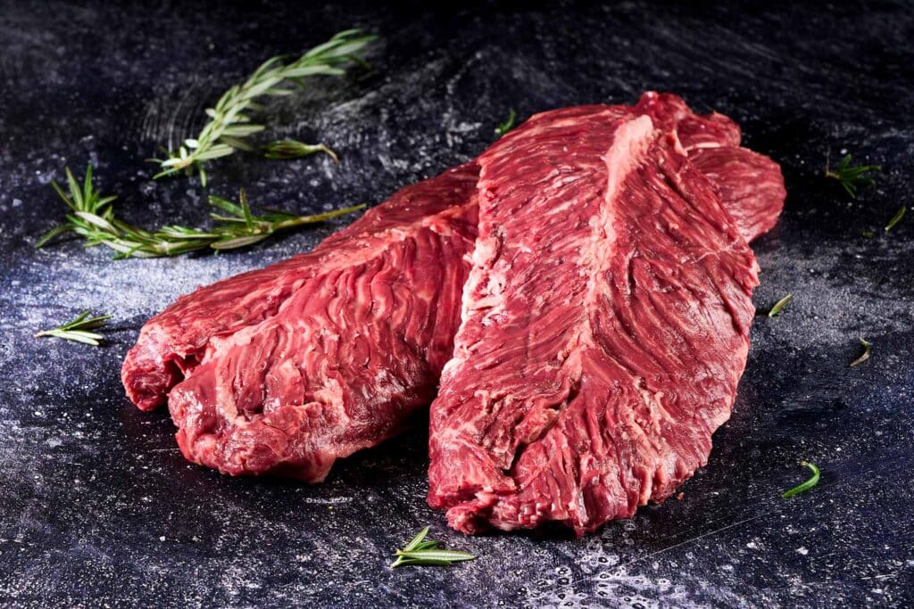 Wagyu Hanging Tender cut with rich marbling, presented on a dark surface with fresh herbs, showcasing its texture and quality for culinary use.