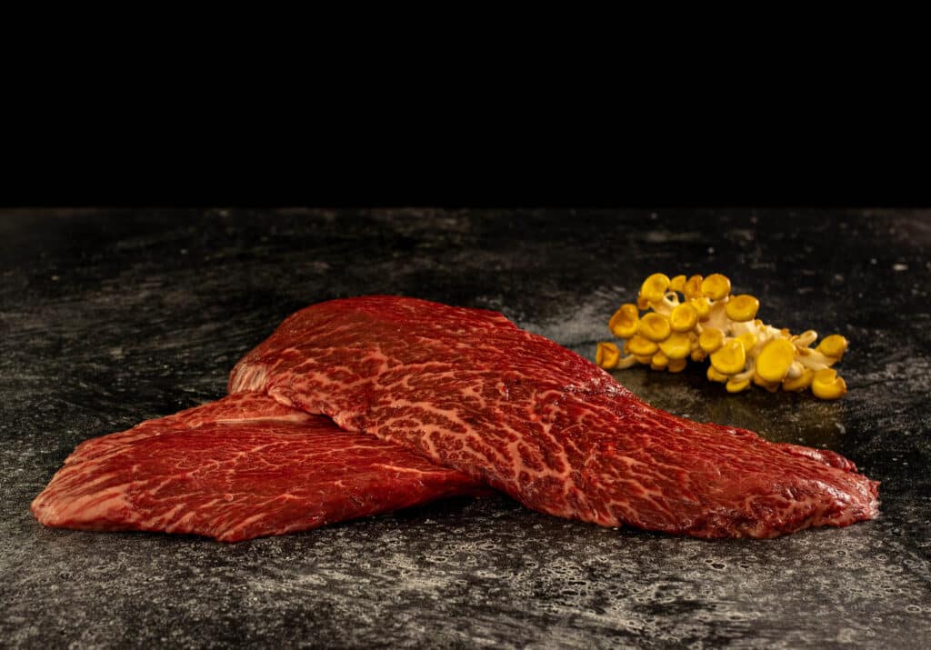 Wagyu Flat Iron steak showcasing rich marbling and deep beef flavor, ideal for high-heat searing, with accompanying roasted nuts in the background.