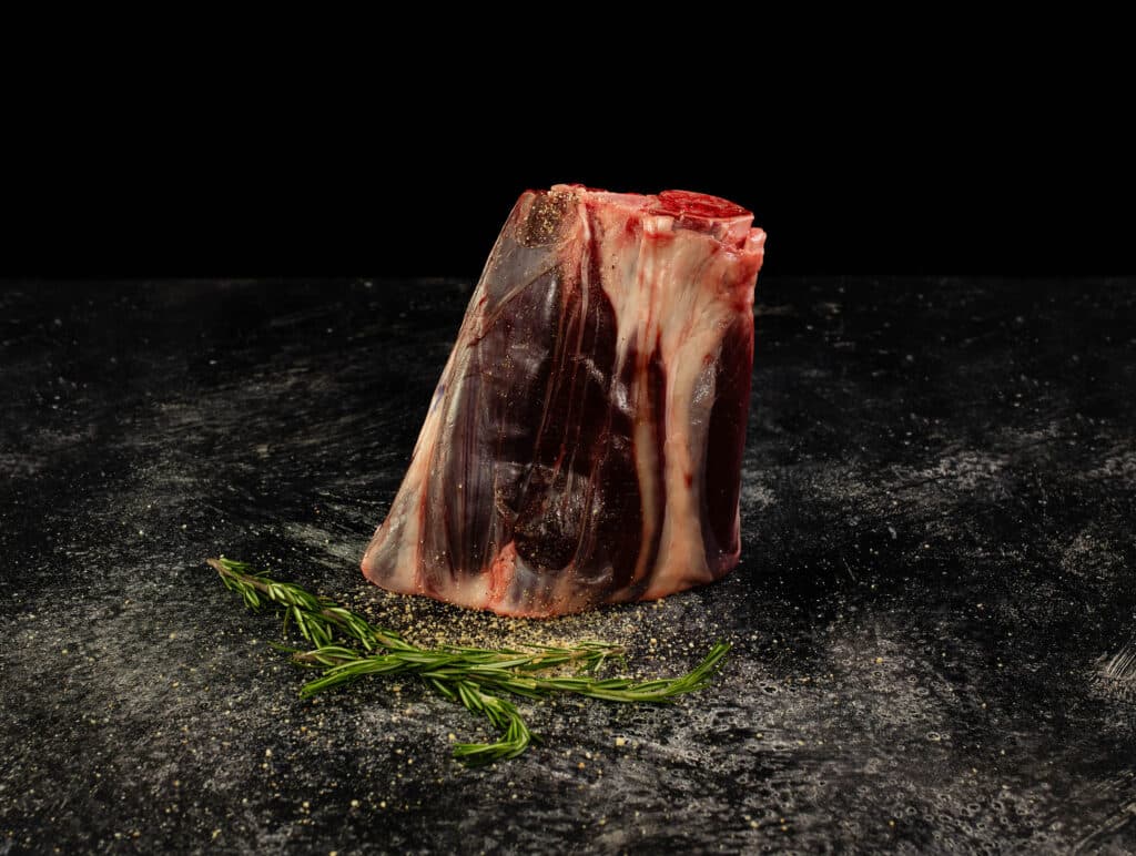 Wagyu foreshank cut displayed on a dark surface, featuring marbled meat and a sprig of rosemary, emphasizing its collagen-rich texture and culinary potential for slow cooking.