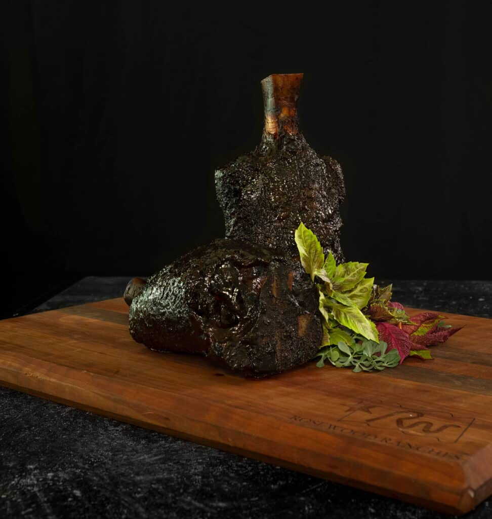 Hind shank cut of premium beef on a wooden cutting board, garnished with fresh herbs, highlighting Rosewood Beef's quality offerings.