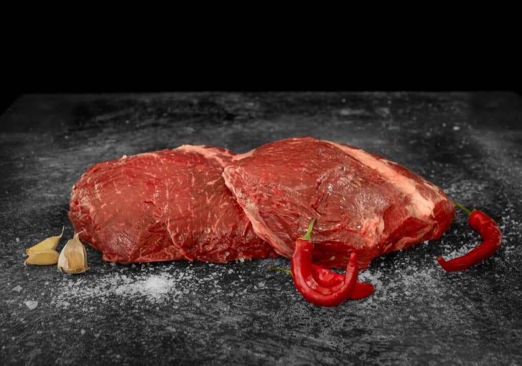 Wagyu sirloin flap cut with rich marbling, accompanied by garlic cloves and red chili peppers on a black surface.